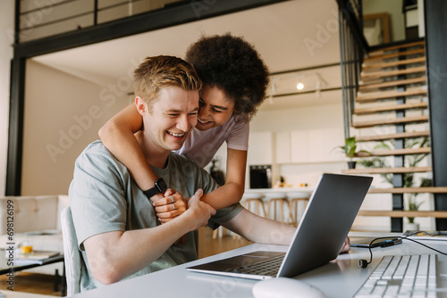 Woman hugging her boyfriend while he working on laptop computer at home photo