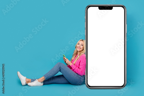 Full length photo of optimistic young girl sit comfort browsing phone internet web page touchscreen advert isolated on blue color background © deagreez