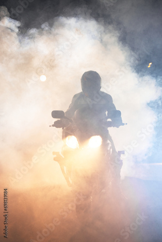 Motorcyclist in a leather jacket suit through the red and blue smoke on a motorcycle at night