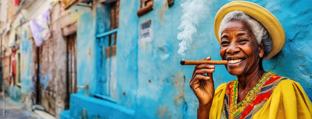 Elderly Woman Enjoying a Cigar Against a Blue Wall in Havana. Smiling Senior Lady in Yellow Dress and Straw Hat with Cigar in Cuba - obrazy, fototapety, plakaty 