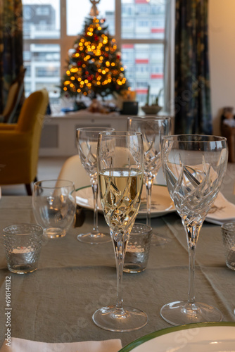 New year dinner served with champagne cava or prosecco wine in crystal glasses on table with christmas tree and garland lights on background