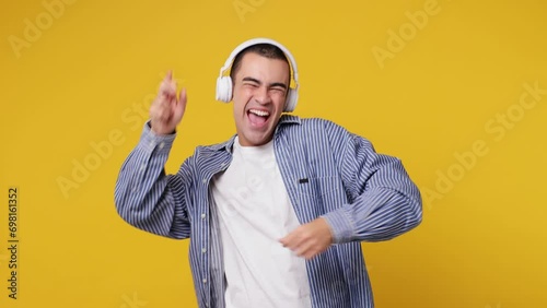 Vivid cheerful calm fun young middle eastern man he wear blue shirt white t-shirt listen mp3 music in headphones slow dance sing song have fun enjoy relax isolated on plain yellow background studio photo