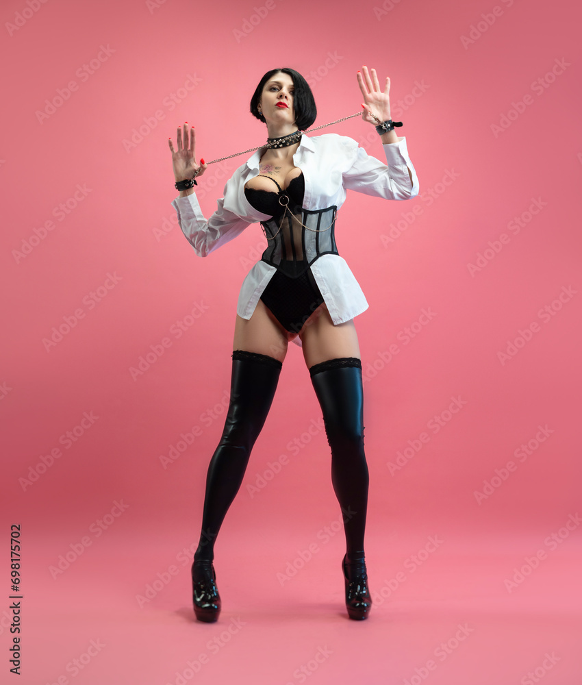 sexy woman with glasses, in a BDSM mistress costume in stockings, posing sexually on a pink copy paste background