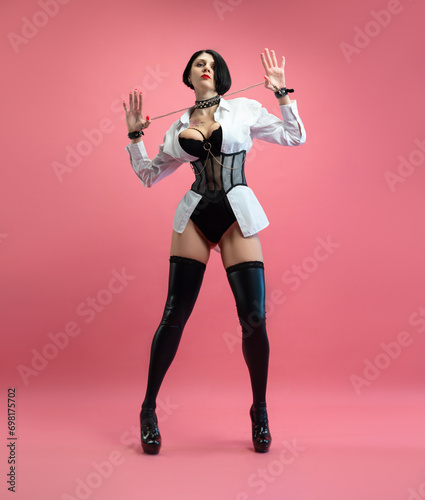 sexy woman with glasses  in a BDSM mistress costume in stockings  posing sexually on a pink copy paste background