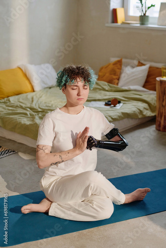 Girl with prosthetic arm keeping hands in mudra when practicing cowface asana at home photo