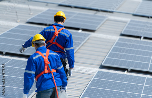 Both of technicians is installing solar panels on the roof of the warehouse to change solar energy into electrical energy for use in factories.