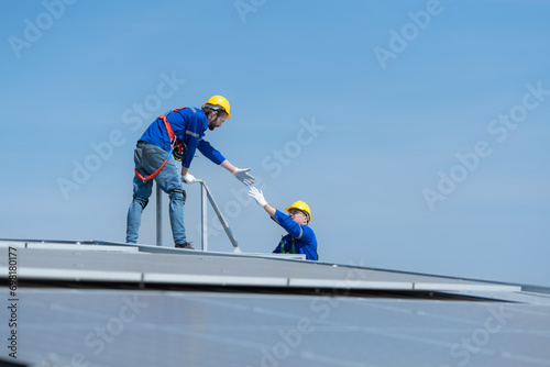 A young technician intern working on solar panels is fear of heights with senior engineers who are always helping out