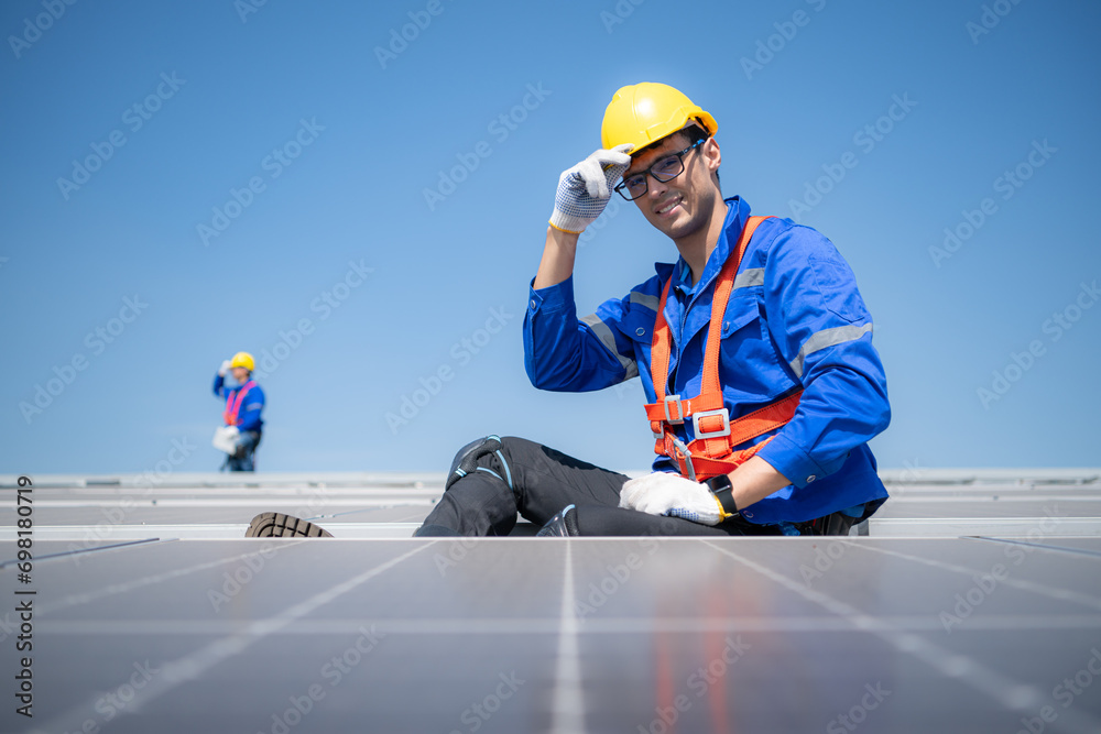 Technician repairing solar panels take off his hat and rest in the scorching sun on a factory roof covered with solar panels to receive solar energy. Technician repairing solar panels take off his hat and rest in the scorching sun on a factory roof covered with solar panels to receive solar energy.