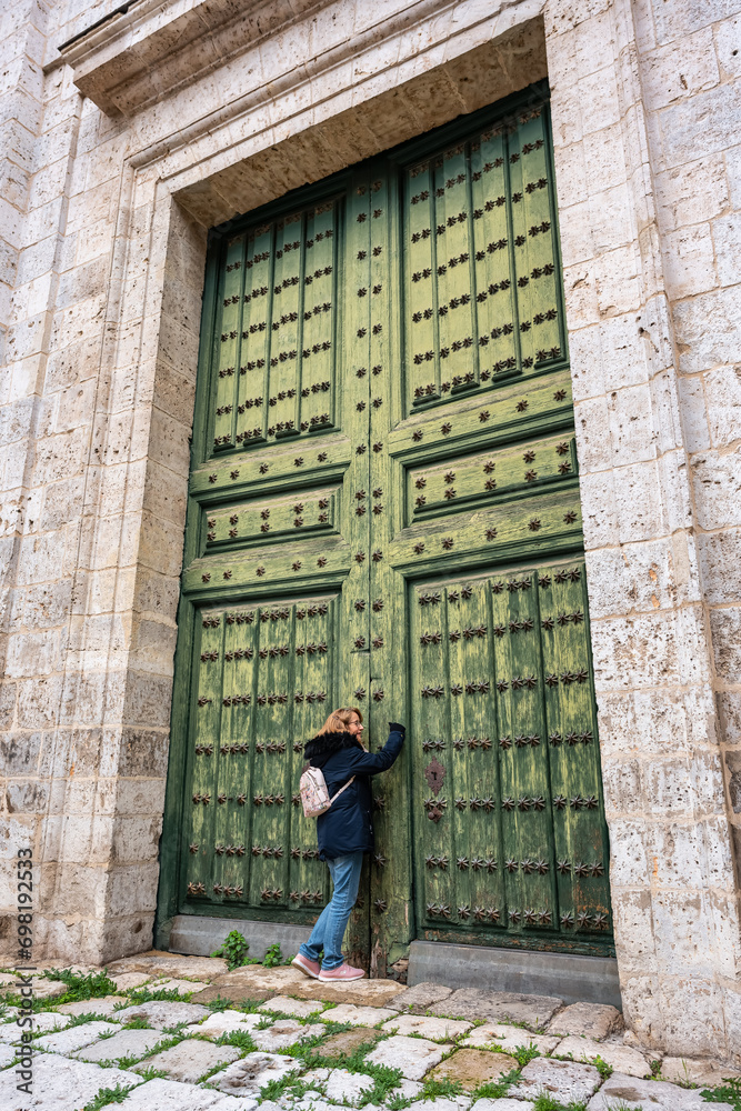 Tourist woman knocking on a huge wooden door of the medieval cathedral of Valladolid.