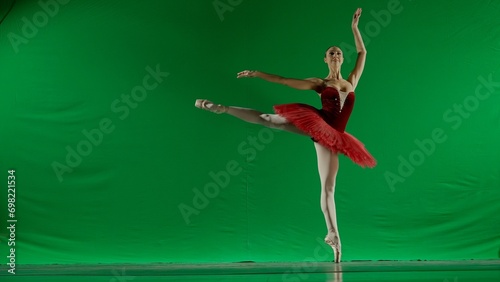Woman on chroma key background of green screen. Beautiful ballerina in red tutu and pointe shoes dancing on toes choreography in studio.