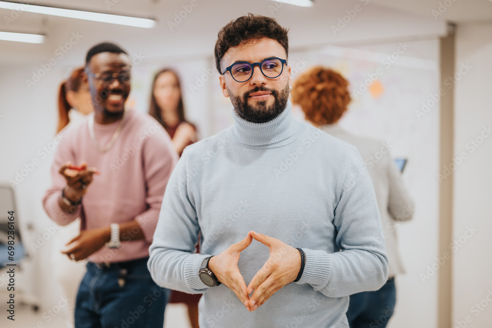 Handsome, male person posing for the camera while his diverse coworkers brainstorming and collaborating for business success in the office in the back. Handsome, male person posing for the camera while his diverse coworkers brainstorming and collaborating for business success in the office in the back.