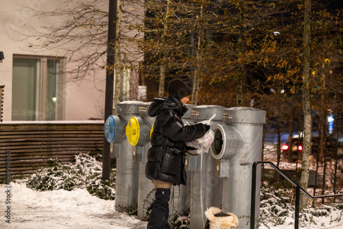 Stockholm, Sweden, A young woman throws garbage in a shute with a dog on a leash in a resdiential complex at night in the winter. photo