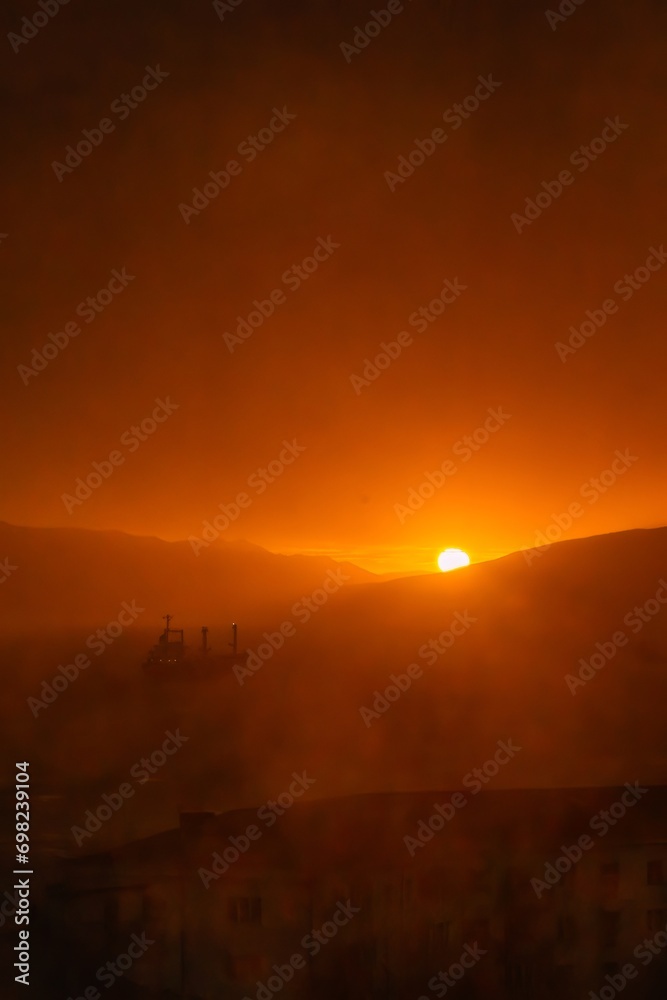 The hour of dawn over the Black Sea near the city of Novorossiysk - the sun, orange light and a large ship in the roadstead - vertical orientation photo