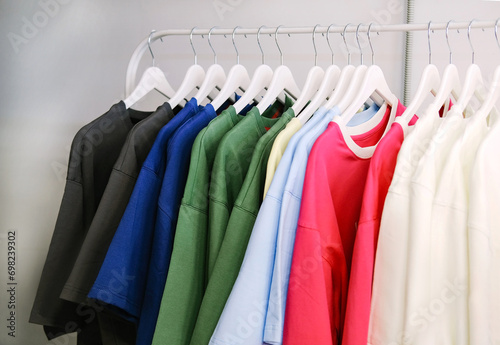 Shopping Concept. Clothing Rail With Bright Trendy Clothes Hanging On Hangers Over White Studio Background In Empty Room. Fashion Trends And Style