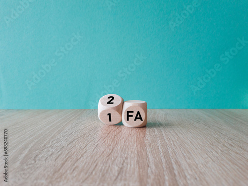 Turned wooden a cube and changes the abbreviation 1FA (One factor authentication) to 2FA (Two factor authentication). Beautiful blue background, wooden table.