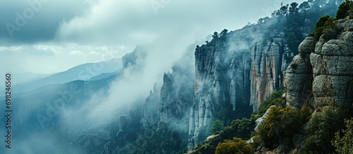 Cloudy and foggy weather surrounds cliffs with trees near Montserrat Abbey in Spain. © AkuAku
