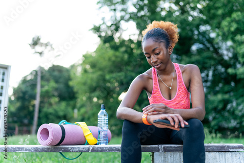 Sitting post-workout, the African American girl checks calories burned on her smartwatch. With determination, she tracks progress, using technology to stay motivated on her fitness journey photo