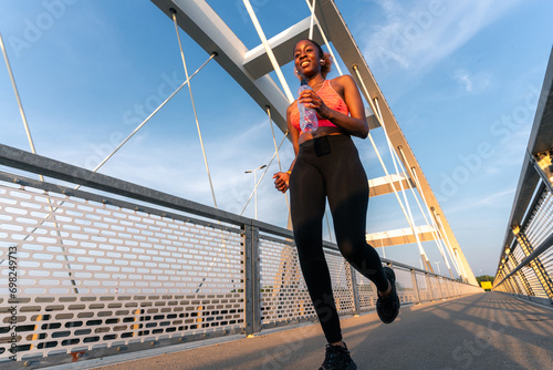 As the sun sets, she runs across the bridge, a bottle in her hand, periodically glancing at her watch. The vibrant hues of the sky mirror her determination. photo