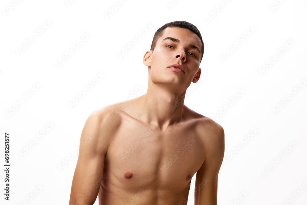 Portrait of brutal, handsome young guy with shirt hair, spotless perfect skin, standing shirtless against white studio background. Concept of male beauty, skin care, spa, cosmetology, men's health