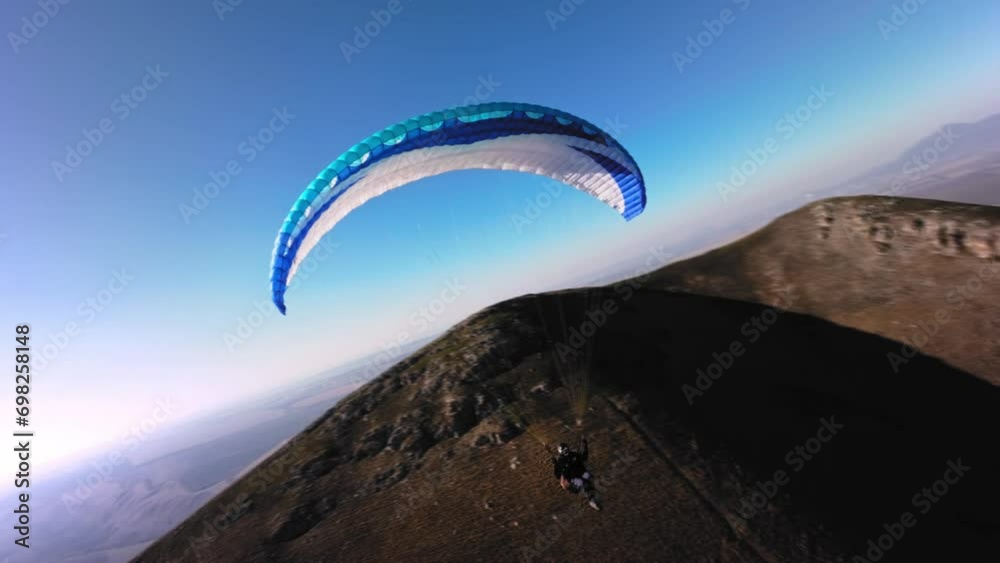 Aerial view from a sports FPV drone. A paraglider athlete flies near the slopes of a small mountain. Free paragliding flight over rural fields in autumn Video from FPV drone