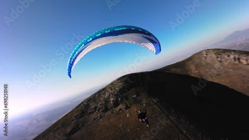 Aerial view from a sports FPV drone. A paraglider athlete flies near the slopes of a small mountain. Free paragliding flight over rural fields in autumn Video from FPV drone