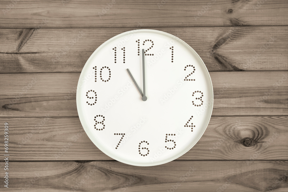 Eleven o'clock. Time management or business concept. Plain white wall clock showing 11 am on a wooden background. Copy space. Opening or closing hours. Schedule or working, study hours. Eleven o'clock. Time management or business concept. Plain white wall clock showing 11 am on a wooden background. Copy space. Opening or closing hours. Schedule or working, study hours.