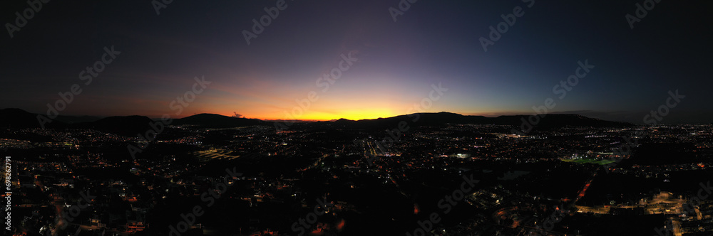 Dusk panorama at a city with night lights and the sky with colors and the sun going down the mountains. Almost night.