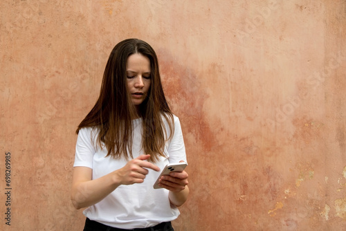 Portrait of a young girl in a white T-shirt with a phone in her hands.