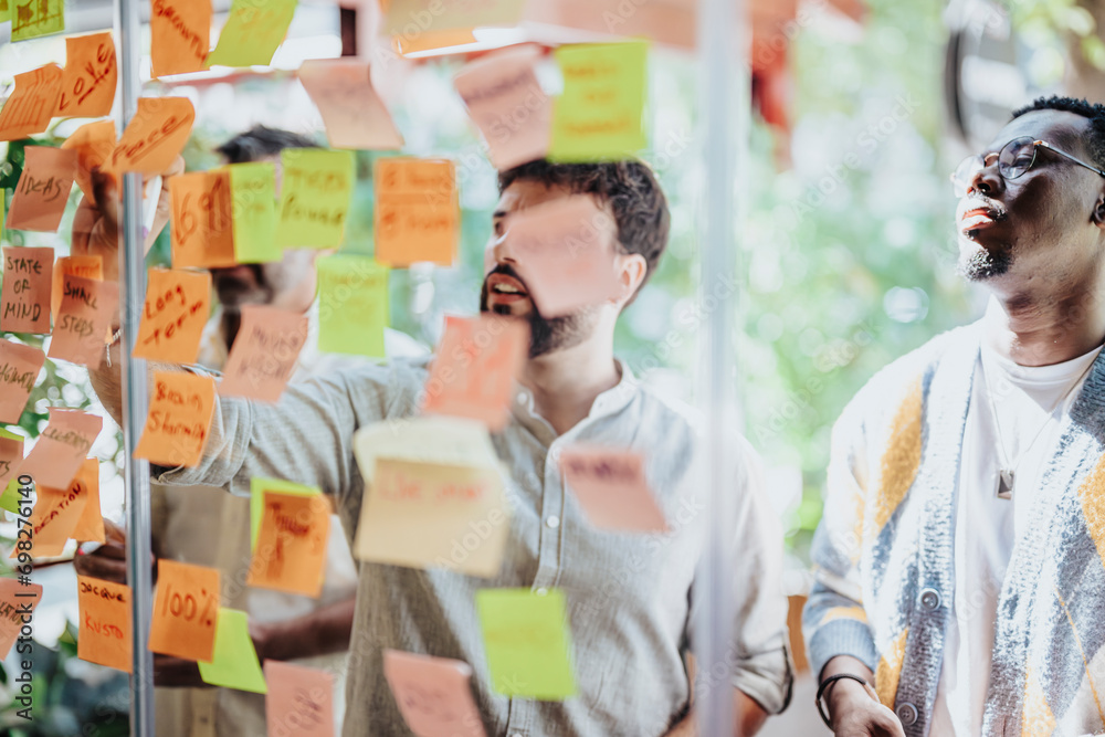 Diverse business partners collaborate in a modern office, brainstorming and planning with post-it notes on a glass wall. Successful teamwork and cooperation in achieving goals. Diverse business partners collaborate in a modern office, brainstorming and planning with post-it notes on a glass wall. Successful teamwork and cooperation in achieving goals.