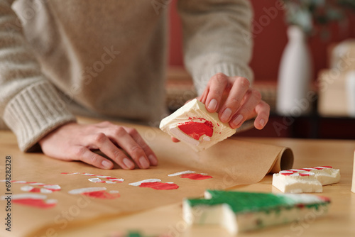 Hands of young unrecognizable woman making prints of Santa cap while holding workpiece over unrolled piece of craft paper
