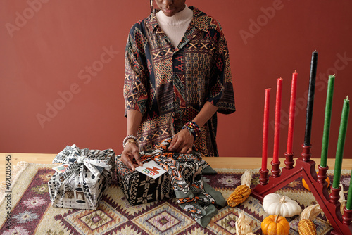 Cropped shot of African American girl putting handmade postcard in giftbox wrap while preparing presents for her family photo