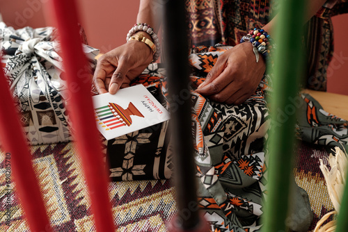 Candleholder with multi-colored candles and hands of young African American woman putting handmade postcard in gift wrap photo