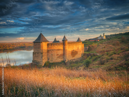 Golden light of sun on grass and walls on fortress under sky with clouds