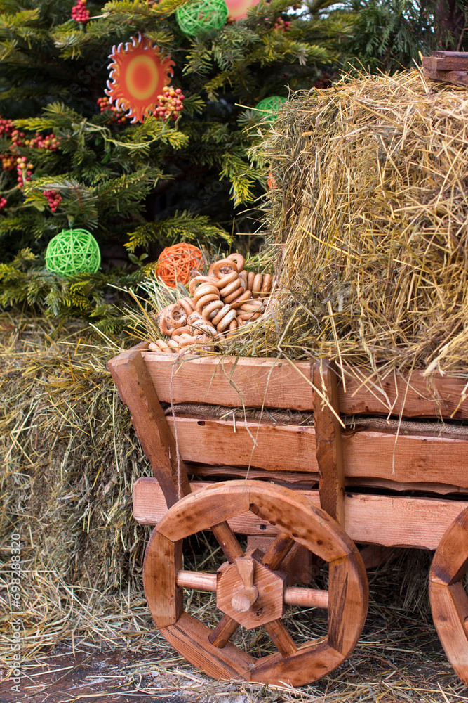 Folk decorations for the Maslenitsa holiday. Wooden cart with hay and bagels, red apples