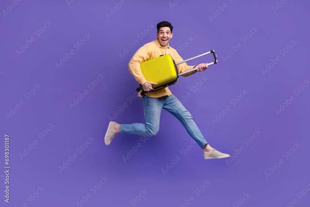 Full body photo of nice young male running hold suitcase traveler dressed stylish yellow outfit isolated on purple color background Full body photo of nice young male running hold suitcase traveler dressed stylish yellow outfit isolated on purple color background