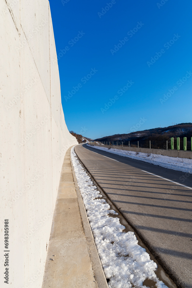 Obraz premium An empty two-lane highway. Winter scene. Empty asphalt road in rural landscape at sunset with blue clouds. Asphalt highway road with beautiful blue sky in pastoral rural environment.