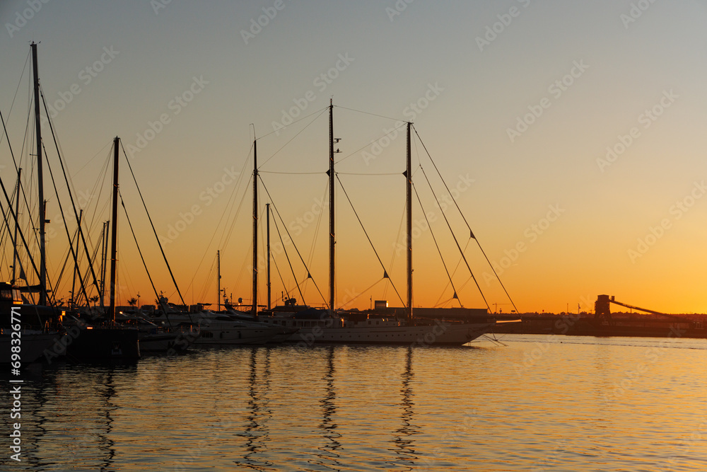 Silhouettes of sailboats and masts in the marina at sunset.