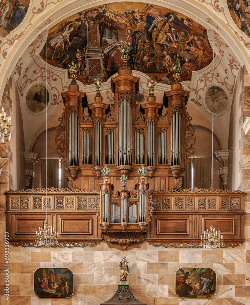 Ornate organ in the Abbey of Ebersmunster, surrounded by striking framed artwork