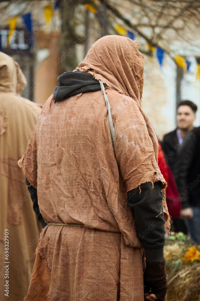 an individual dressed in a large brown hoody is walking through the crowd
