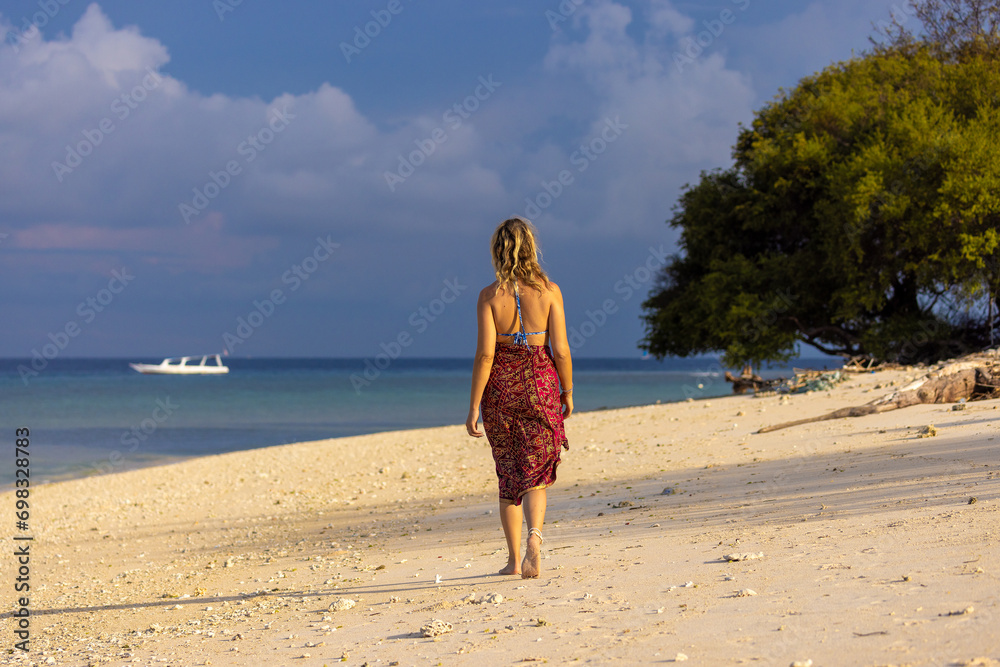 A young woman is walking on a sand beach in Gili Meno, Indonesia A young woman is walking on a sand beach in Gili Meno, Indonesia