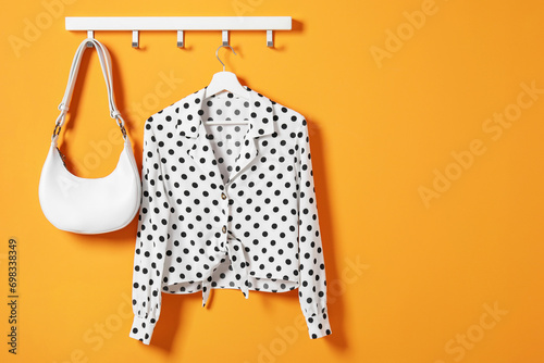 Hanger with polka dot shirt and bag on orange wall, space for text photo