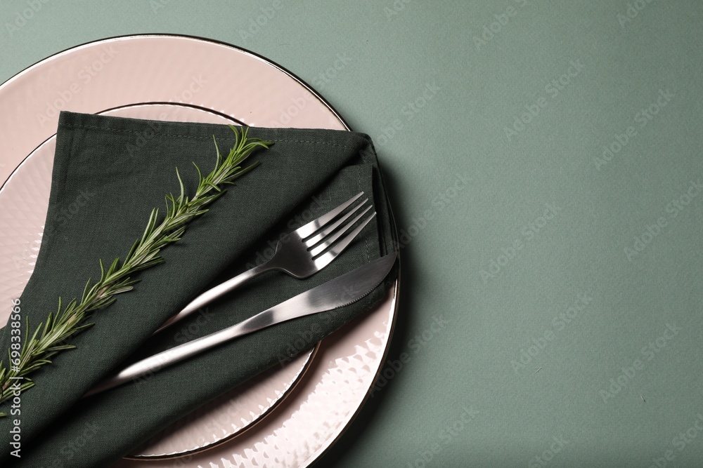 Stylish table setting. Plates, cutlery, napkin and rosemary on green background, top view with space for text - obrazy, fototapety, plakaty 