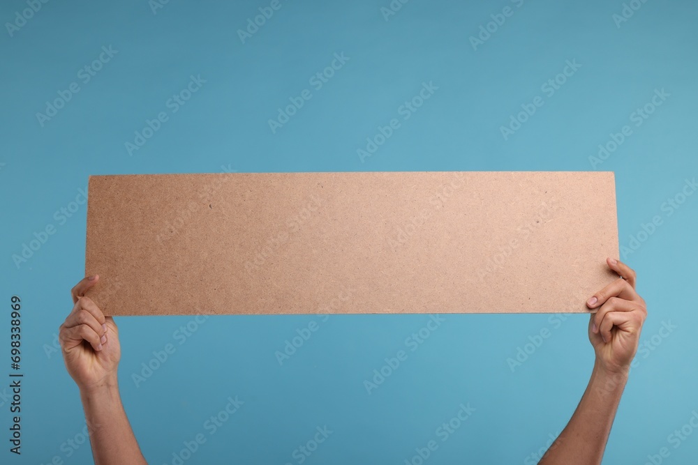 Man holding blank cardboard banner on light blue background, closeup. Space for text Man holding blank cardboard banner on light blue background, closeup. Space for text