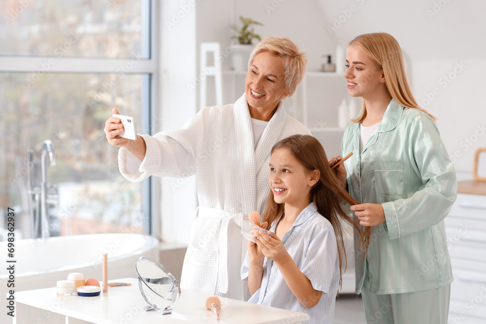 Fototapeta premium Little girl with her mom and grandmother taking selfie in bathroom
