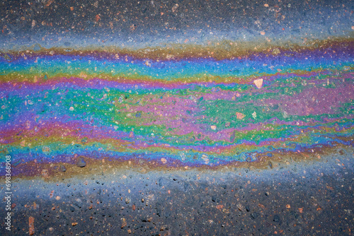 Multi-colored poisonous spots of spilled gasoline on wet pavement during rain. © AleksFil