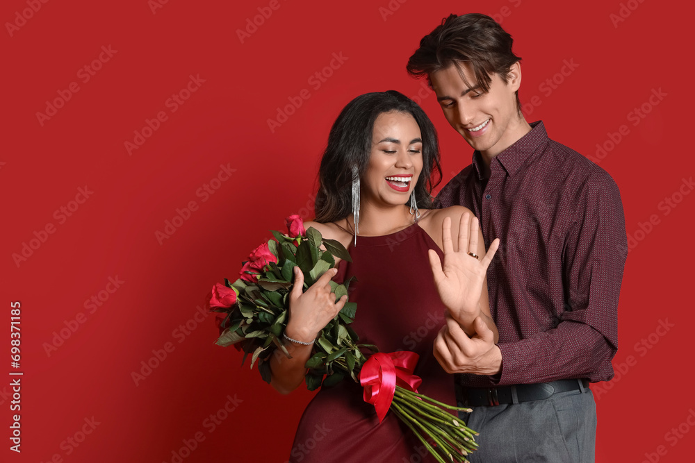 Engaged young couple with ring and roses on red background. Valentine's Day celebration Engaged young couple with ring and roses on red background. Valentine's Day celebration