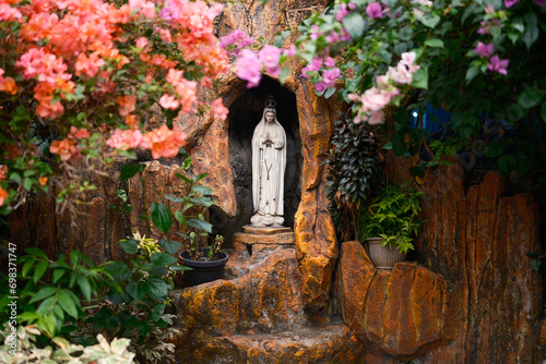 Statue of the Virgin Mary framed with beautiful colors of flowers in the park