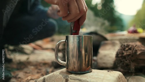 A metal tourist mug on a stone on the background of a bonfire. A mug with a hot drink close-up outdoors on a camping trip. photo