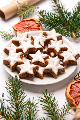 Plate of star-shaped gingerbread cookies with fir branches and dried orange on white background
