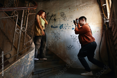 Young man photographing girlfriend on steps in old building